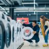 Multicultural Couple Evaluates Washing Machine Choices at Home Electronics Store. Man and Woman in Search of a Reliable Laundry Appliance. Customers Explore Modern Laundry Solutions in Retail Shop
